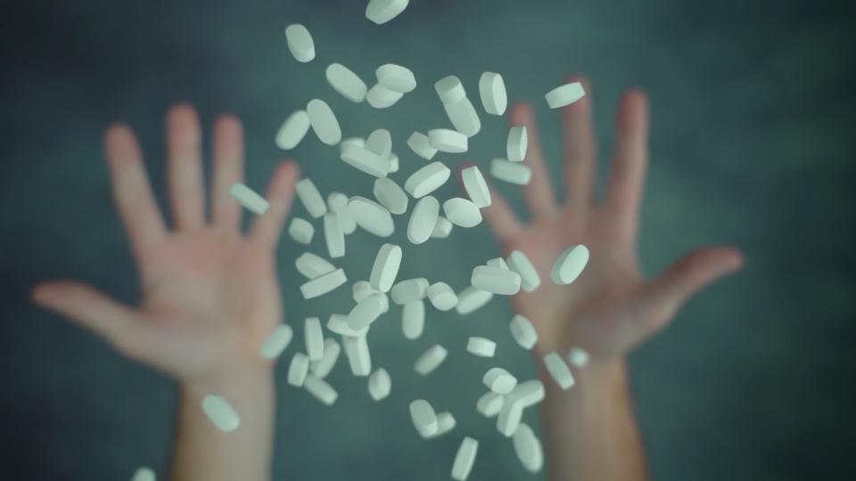 Both hands throwing up handful of pills above table surface