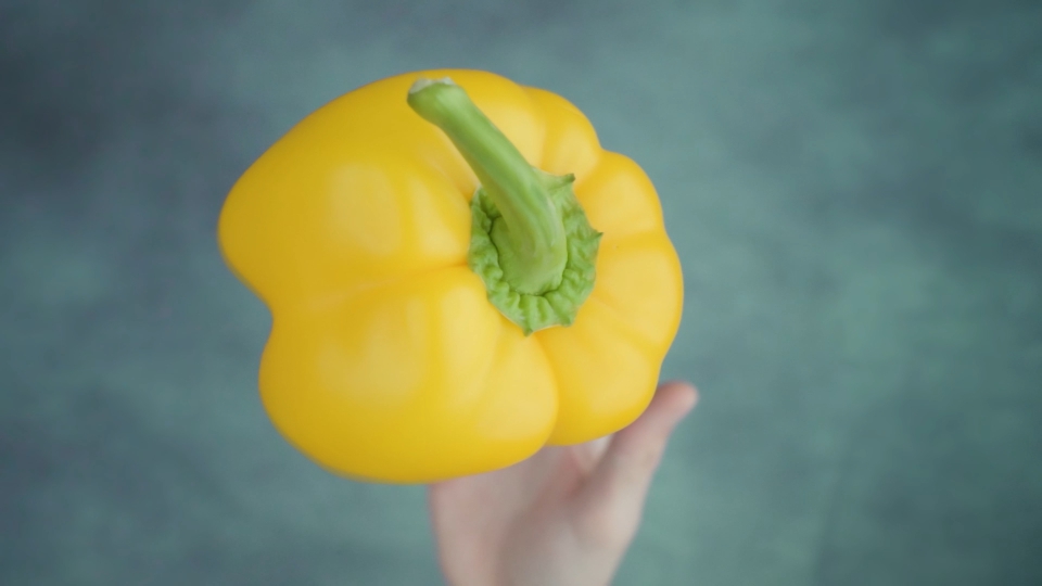 Person throws up uncooked yellow bellpepper above table