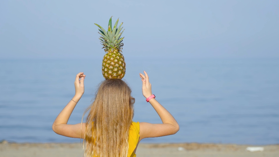 Girl on the beach balances a pineapple on the head