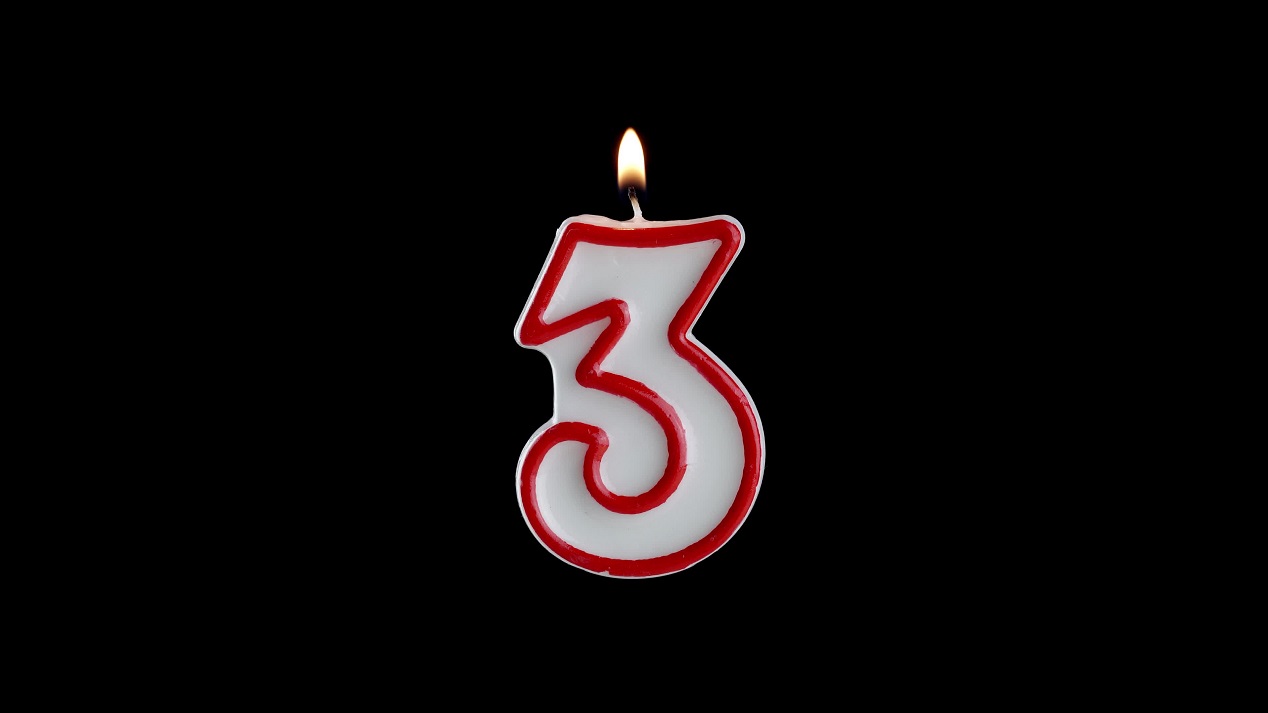 Candle in the shape of the number three on a black background