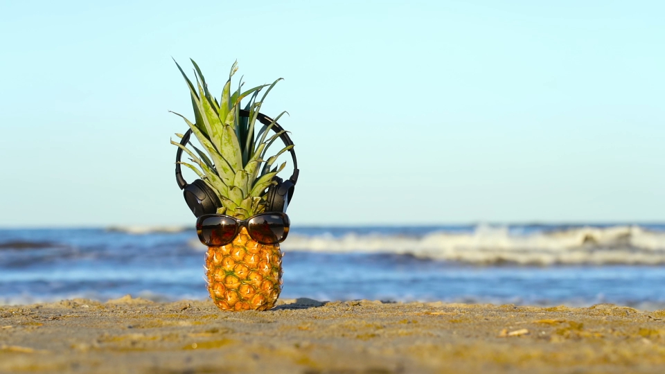 Ananas con occhiali e cuffie sulla sabbia del mare