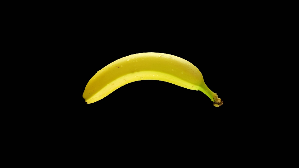 Banana wet by drops of water rotates on isolated black background