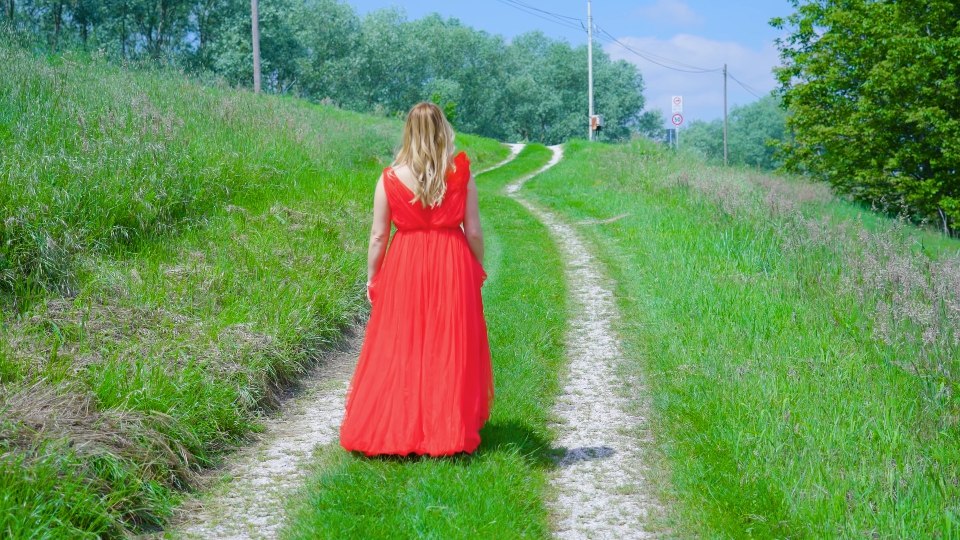 Woman in red dress walks on the dirt road